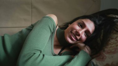 Orta Doğulu genç bir kadın büyük bir gülümsemeyle kanepede yatarken dinleniyor. 20 'li yaşlarda dinlenen bir Arap kızı.