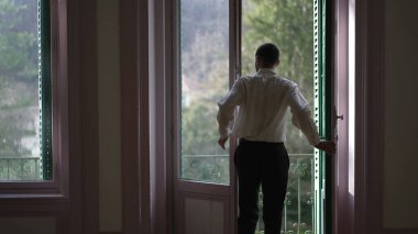 Geniş pencereler açan, balkona çıkan, temiz havanın tadını çıkaran ve düşüncelere dalmış birinin arka planı.