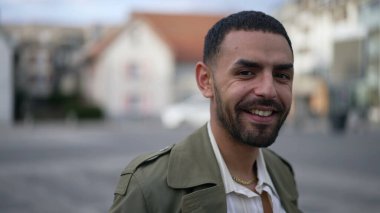 Şehirde yürüyen kendine güvenen bir Faslı. Kentsel çevrede gülümseyen Arap bir erkeğin hareket halindeki görüntüsü