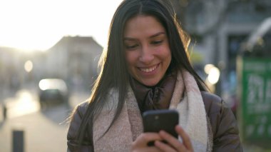 Şehir caddesinde telefona bakan mutlu bir Orta Doğulu genç kadın. 20 'li yaşlarda bir kadın, şehir merkezinde elinde teknoloji cihazıyla dikiliyor.