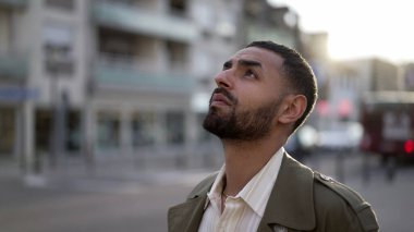 Sokakta dikilen düşünceli bir Orta Doğulu genç gökyüzüne umutla ve inançla bakıyor. Gülümseyen yüz yukarı doğru dönüyor.