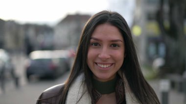 Genç, kendine güvenen esmer bir kadının portresi kameraya doğru gülümseyerek yürüyor. Mutlu, yetişkin bir kız. Sokakta ağır çekimde yakın çekim yüzü.