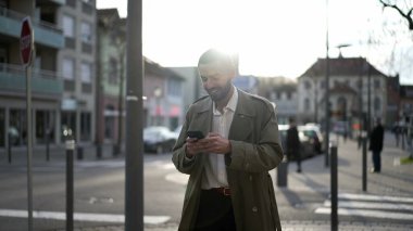 Şehirde yürüyen mutlu bir Faslı genç adam cep telefonuna gülümsüyor. Erkek bir Orta Doğulu gün batımında bir işaret fişeğiyle kaldırımda yürür.