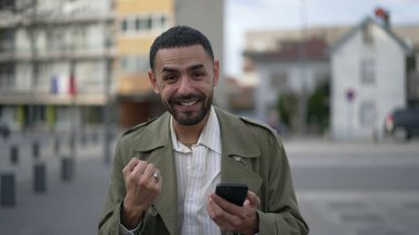 Orta Doğulu bir adam elinde cep telefonu cihazıyla internetten içeriği seviyor. Bir Arap, şehir caddesinde dikilirken mesaja olumlu tepki veriyor.