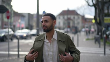 Şehirde yürüyen kendine güvenen bir Faslı. Kentsel çevrede gülümseyen Arap bir erkeğin hareket halindeki görüntüsü