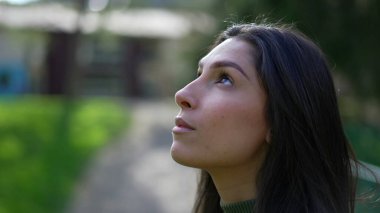 Düşüncelere dalmış genç bir kadının gülümseyerek gözlerini açması... Umutla ve inançla parkın dışında dururken...