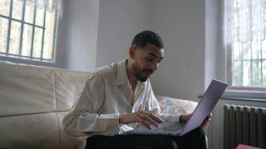 Heyecanlı bir Orta Doğulu genç adam dizüstü bilgisayarın önünde kanepede otururken internetteki başarılı mesaja olumlu tepki veriyor.