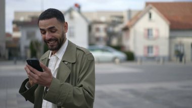 Orta Doğulu bir adam elinde cep telefonu cihazıyla internetten içeriği seviyor. Bir Arap, şehir caddesinde dikilirken mesaja olumlu tepki veriyor.