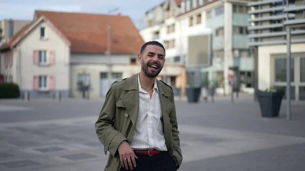 One happy Middle Eastern man smiling and laughing while standing outside in city street. Authentic real life laugh and smile of a Middle Eastern male person