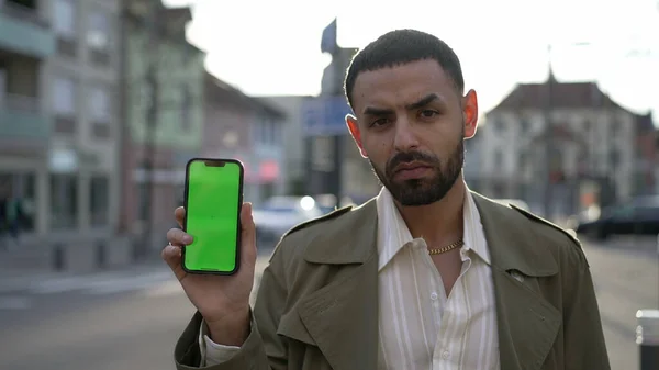 外の街の通りに立っている間 ディスプレイ上のクロマグリーンとスマートフォンの画面を示す一人の深刻なアラブの若者 — ストック写真