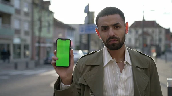 外の街の通りに立っている間 ディスプレイ上のクロマグリーンとスマートフォンの画面を示す一人の深刻なアラブの若者 — ストック写真