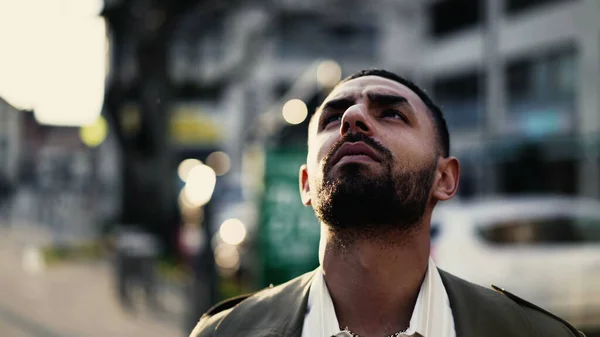 一个沉思的阿拉伯年轻人站在街上看着天空 有着精神上的体验 一名中东男子的近视脸站在室外城市环境中跟踪射击 — 图库照片