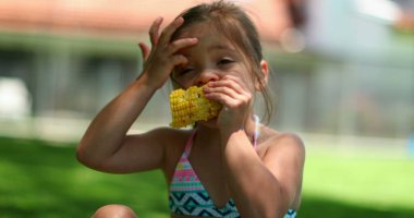 Arka bahçede mısır yiyen bir çocuk. Küçük kız sağlıklı mısır koçanı yiyor.