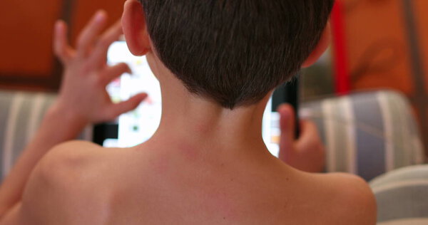 Child playing video-game on tech tablet device. Back of young boy browsing online