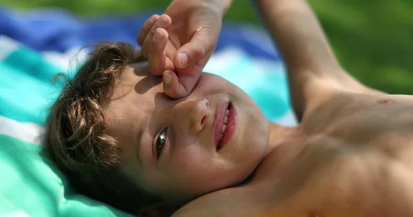 Pensive young boy laid outside in nature, child rubbing eye daydreaming