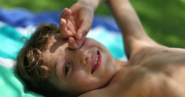 Pensive young boy laid outside in nature, child rubbing eye daydreaming