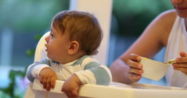 Mother feeding baby infant son toddler on highchair
