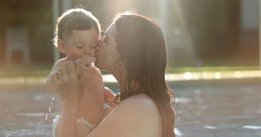 Mother caring for baby at the swimming pool kissing on the cheek, mom kisses toddler