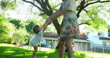 Mom playing with baby child outside in home garden, mother spinning with toddler