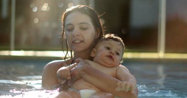 Mother with baby at the swimming pool splashing water with feet