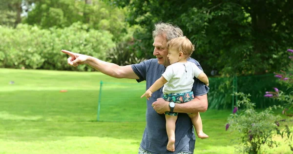 Großvater Zeigt Mit Hand Und Arm Während Enkel Draußen Hält — Stockfoto