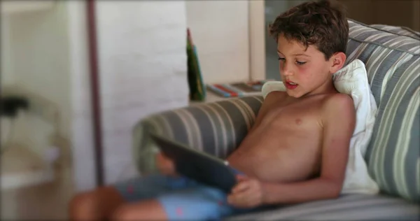 家庭用ソファでタブレットデバイスでビデオゲームをプレイする子供 — ストック写真