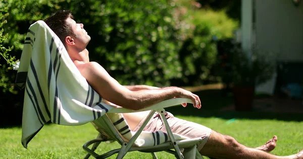 Man sunbathing outside in home lawn. Person outdoors relaxing