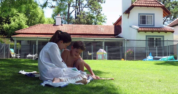 裏庭の家の芝生で読むことを子供の息子を教える母親 — ストック写真