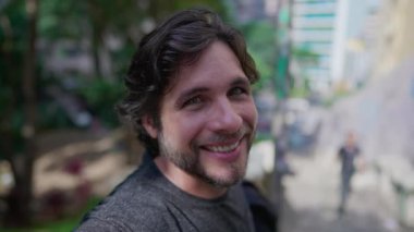 Şehir parkında durmuş gülümseyen kameraya bakan yakışıklı bir gencin portresi. 30 'lu yaşlarda mutlu bir erkek.