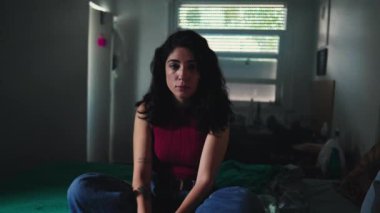 Ciddi bir yüz ifadesi olan genç bir kadın karanlık bir yatak odasındaki kameraya yakından bakıyor. 30 'lu yaşlarda bir kadının dramatik kontrastı