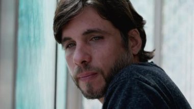 Düşünceli bir genç adam pencerenin kenarına eğilmiş düşünceli bir ifadeyle. 30 'lu yaşlardaki erkek, hayatı yakından düşünüyor.