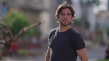 Bir milenyum adamı şehrin dışında durmuş kameraya bakıyor doğal ifadesiyle ve günlük kıyafetleriyle.