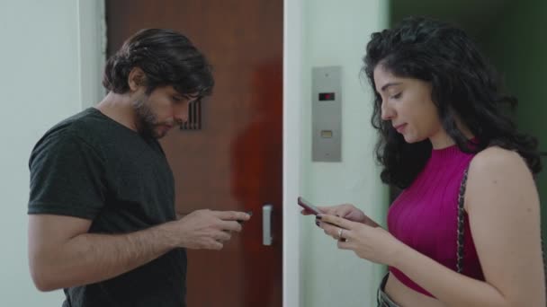现代夫妇在等电梯的时候看着他们的手机 男人和女人出去检查他们的手机打发时间 — 图库视频影像