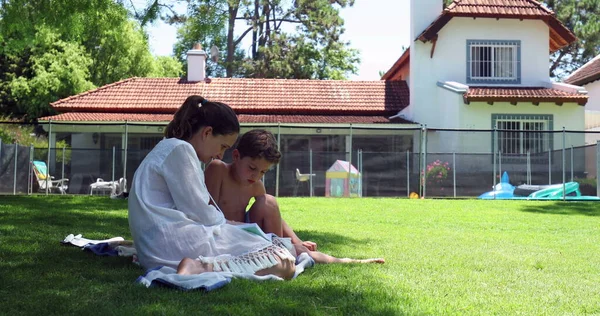 裏庭の家の芝生で読むことを子供の息子を教える母親 — ストック写真