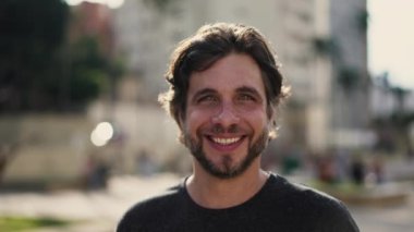 Şehir parkında kameraya gülümseyen genç ve mutlu bir adamın portresi. 30 'lu yaşlarda beyaz bir erkek kameraya bakıyor.