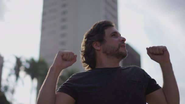 Счастливый Человек Празднует Победу Поднимая Оружие Стоя Городском Парке Отслеживающий — стоковое видео