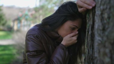 Ağaca yaslanmış acı çeken genç bir kadın çaresiz hissediyor. 20 'li yaşlardaki yetişkin bir kız zor zamanlarda yüzünü utanç ve pişmanlıkla örtüyor.