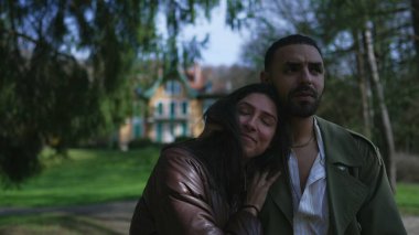 Orta Doğulu bir çift, güzel güneşli bir günde, parkın içinde gülücükler saçan ve şefkatle kucaklaşan bir şekilde geziniyorlar.