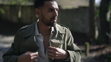 Genç, modaya uygun bir Arap adam dışarıda duruyor ve ceketini düzeltiyor.