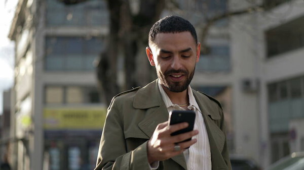 One happy Arab young man closeup face smiling while holding cellphone device standing in street. Closeup face of a male Middle Eastern person smiling and using technology