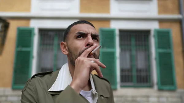 思いやりのある表情で外でタバコを吸っているある重大な中東の若者 横たわりしながら顔を撃たれた — ストック写真