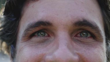 Kameraya yakından bakan bir erkek yüzü. 30 'lu yaşlarda kırışık ve yeşil gözlü bir adam hafif bir gülümseme.