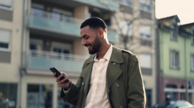 Şehir caddesinde cep telefonu kullanan biri. Gülümseyen ve elinde telefon mesajı ya da sosyal medya mesajı tutan bir adamın görüntüsü