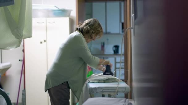 一位老妇人站在洗衣房熨烫衣服 老年人在家里做日常家务活 真正的家庭生活 — 图库视频影像