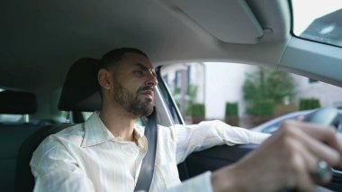 Düşünceli bir ifadeyle direksiyonun başına odaklanmış Orta Doğulu bir sürücü. Dikkatli ve dikkatli bir şekilde araba süren bir Arap. Direksiyon başında düşünceli bir şekilde duran genç bir adamın iç çekimi.