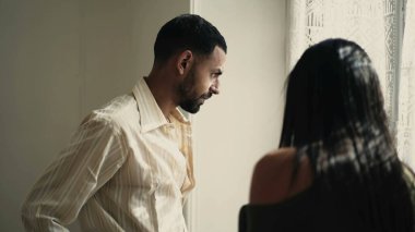 Kızgın adam evde pencerenin önünde kız arkadaşıyla tartışıyor. Erkek kişi, partneriyle sorunları tartışırken hayal kırıklığı ve endişe içinde kollarını kaldırıyor