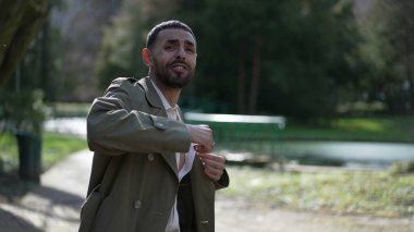 Genç Arap Adam güneşli bir günde parkta dans ederken ceketiyle neşe ve başarı içinde güneşleniyor.