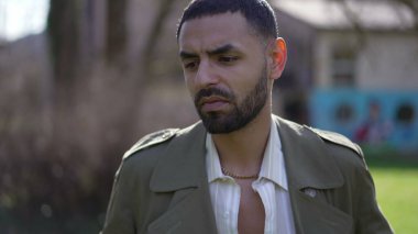 Düşünceli genç bir Orta Doğulu parkın dışında durup düşünüyor. Dalgın bir Arap erkeğinin yakından çekilmiş yüzü.