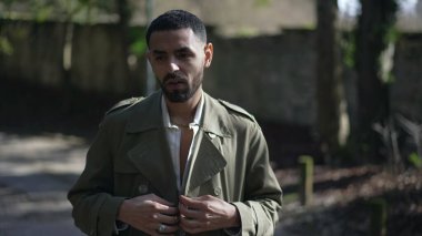 Genç, modaya uygun bir Arap adam dışarıda duruyor ve ceketini düzeltiyor.