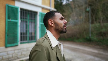 Ciddi bir Arap adam dışarıda düşünceli bir şekilde beklerken sigara yakıyor.